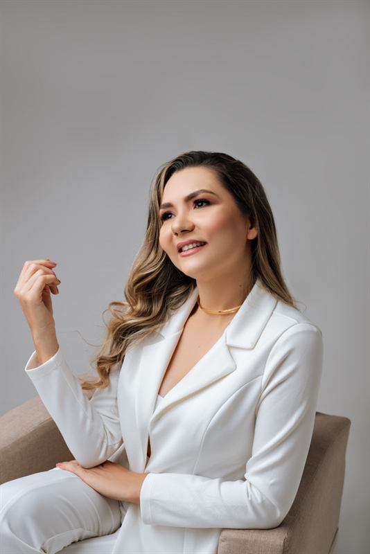 Val Ribeiro sentada em poltrona, em traje branco
